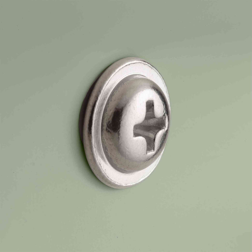 Close-up of a shiny metal Phillips-head bolt with a domed, ridged washer-style head, shown against a plain sage green background.