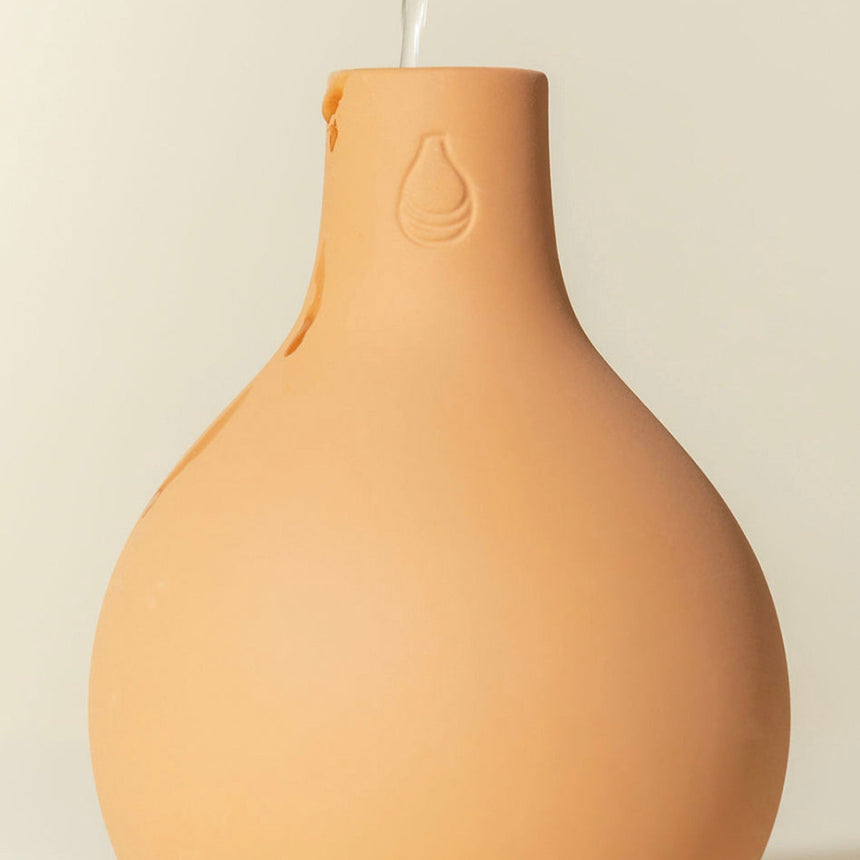 Terracotta Garden Oya watering pot with a bulbous, unglazed body and narrow neck etched with a small water-drop symbol, a clear tube inserted at the top for refilling.