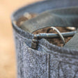 Close-up of a grey felt grow bag filled with soil, showing a drip irrigation elbow fitting and tubing threaded through the fabric rim.