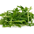 Loose pile of freshly harvested arugula leaves with deeply lobed, jagged edges and pale green stems, shown against a plain white background.