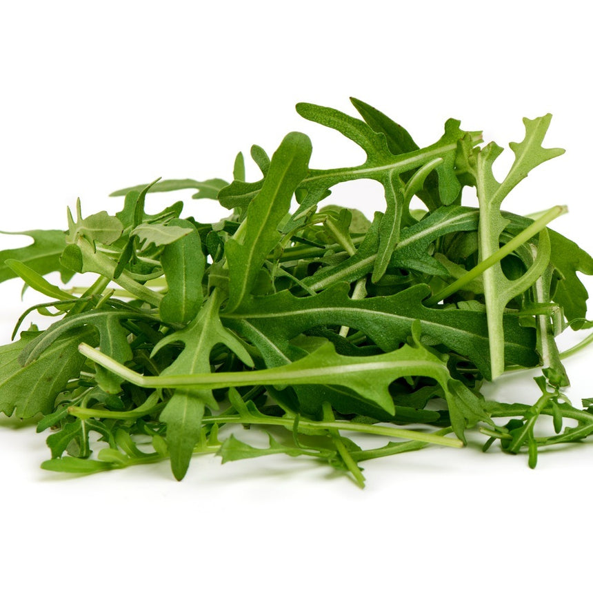 Loose pile of freshly harvested arugula leaves with deeply lobed, jagged edges and pale green stems, shown against a plain white background.