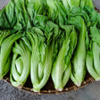 Freshly harvested gai choy mustard greens with pale, crinkled stalks and broad green leaves arranged in rows on a woven bamboo basket.