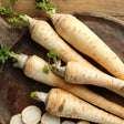 Close-up of freshly harvested, cream-colored Javelin parsnips with leafy green stems, displayed on a wooden plate alongside sliced parsnip rounds.