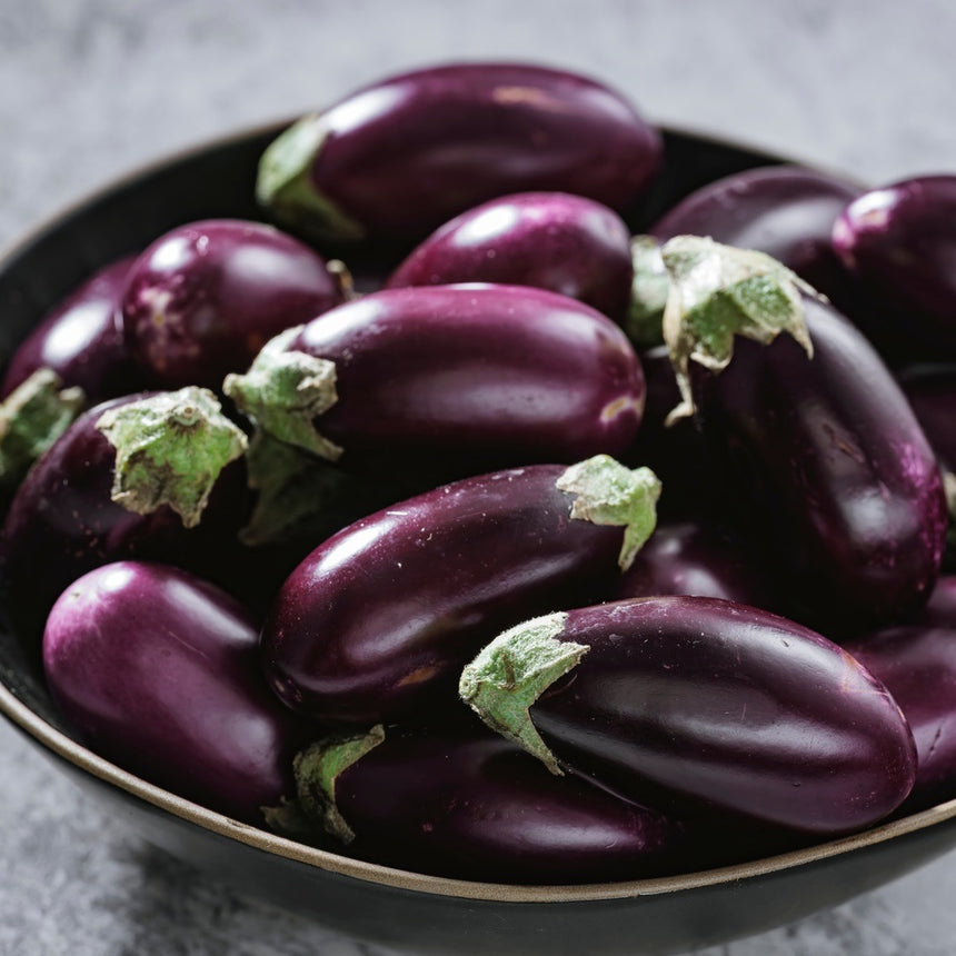 Small oval eggplants with glossy deep-purple skin and pale green stem caps, piled together in a black bowl.