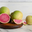 Whole watermelon radishes with pale green-and-white skin arranged on a wooden dish, with one halved and one wedge cut open to reveal vivid pink, radiating flesh inside.