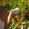 Person holding Midwest Prairie Splendor Flower Mix Seed Shaker canister in a garden setting