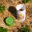 Opened Songbird Delight Flower Mix Seed Shaker canister on a bed of straw with plants around them