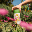 Person holding a Botanical Interests Songbird Delight Flower Mix Seed Shaker canister in a garden with flowers and plants.