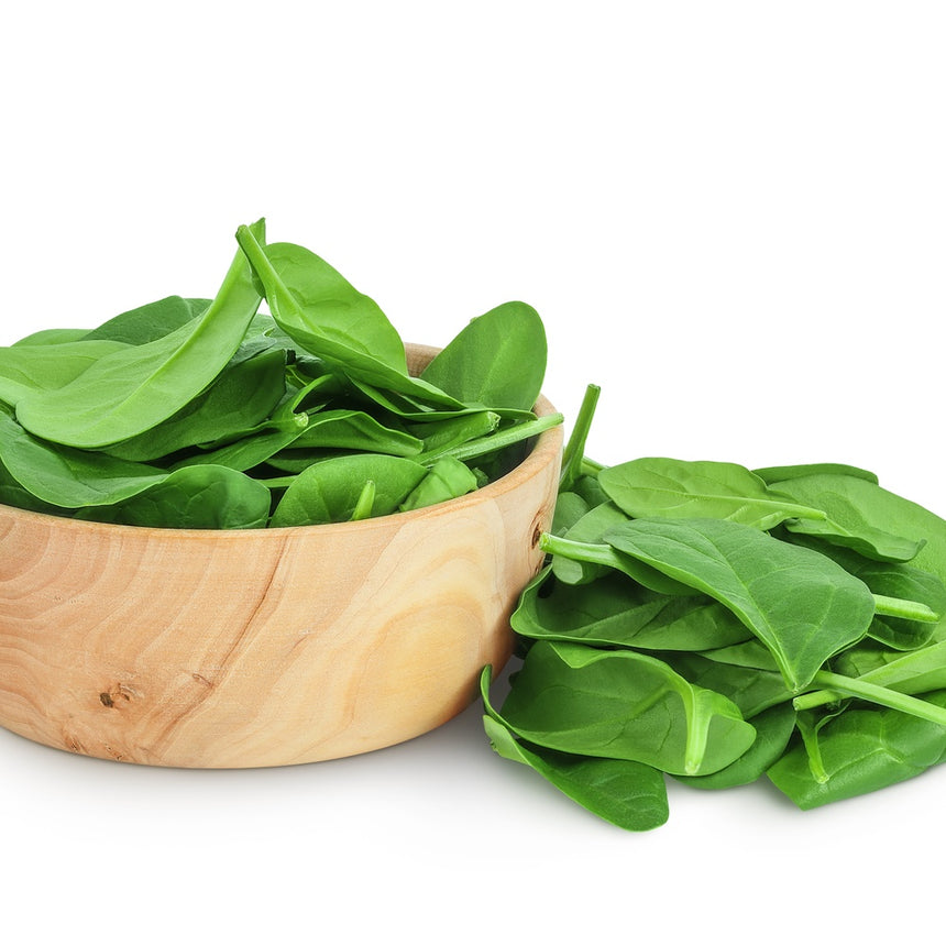 Fresh baby spinach leaves heaped in a wooden bowl with a loose pile spilling beside it on a white background.