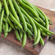 Freshly harvested Tavera filet bush beans, slender and glossy with visible water droplets, piled on a dark wooden board against a stone surface.