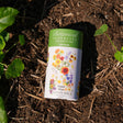 Botanical Interests Water Wise Flower Mix Seed Shaker canister on soil with plants around
